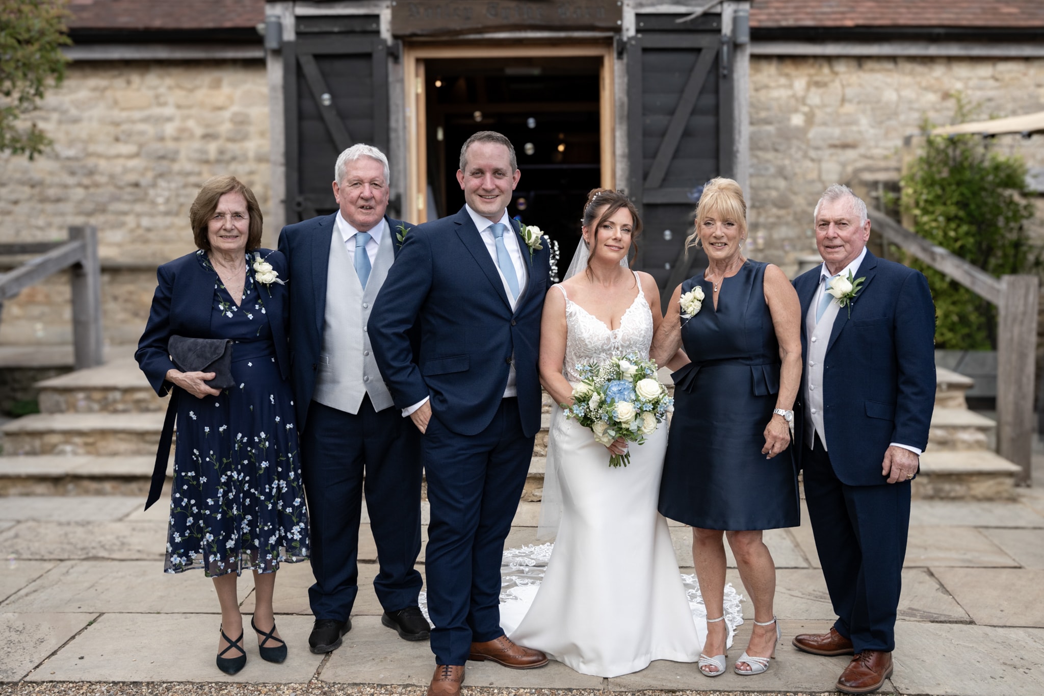 Bride and groom with family group portrait outside Notley Tythe Barn stone entrance