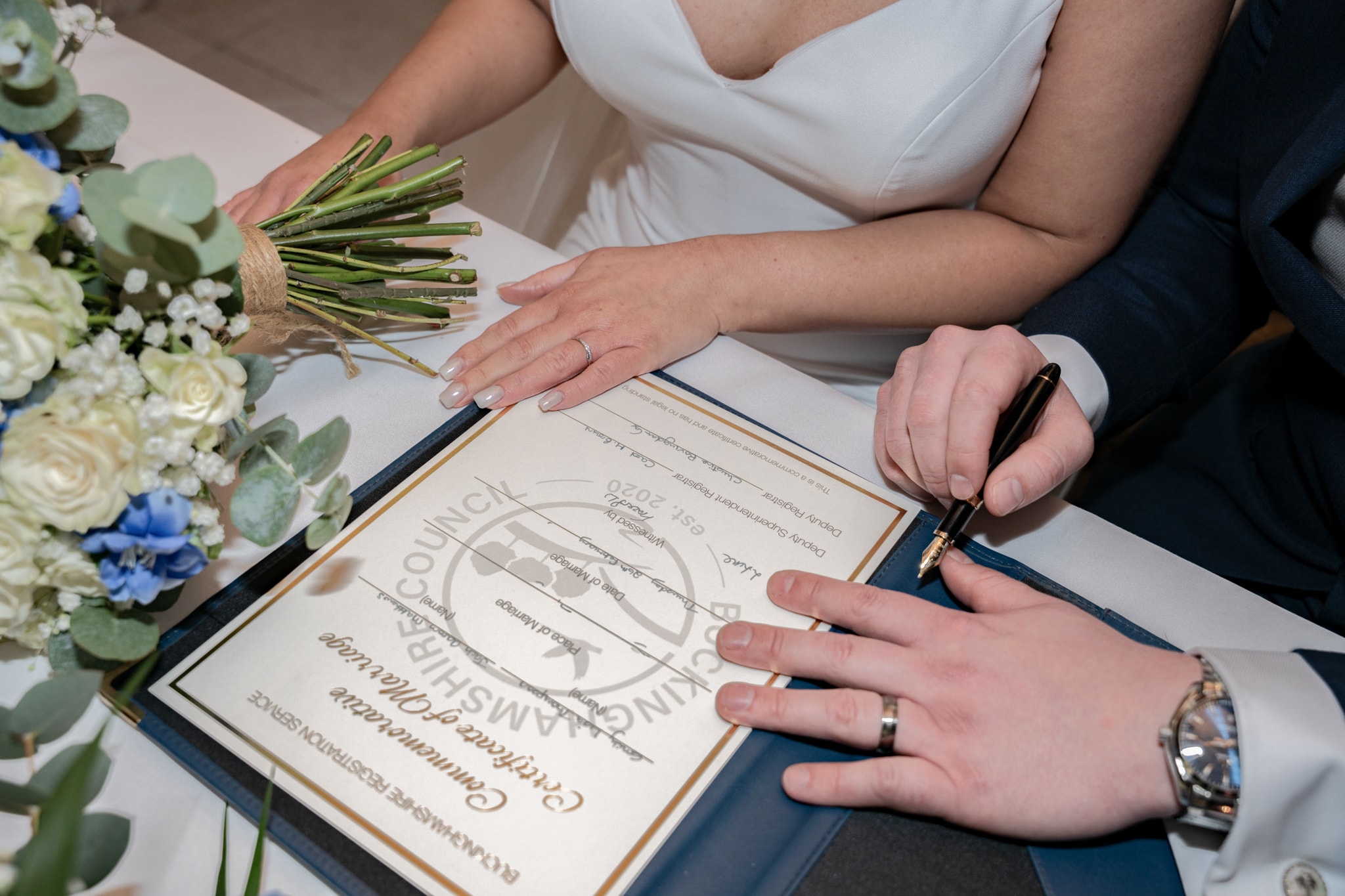 Close-up of bride and groom signing the marriage certificate at Notley Tythe Barn