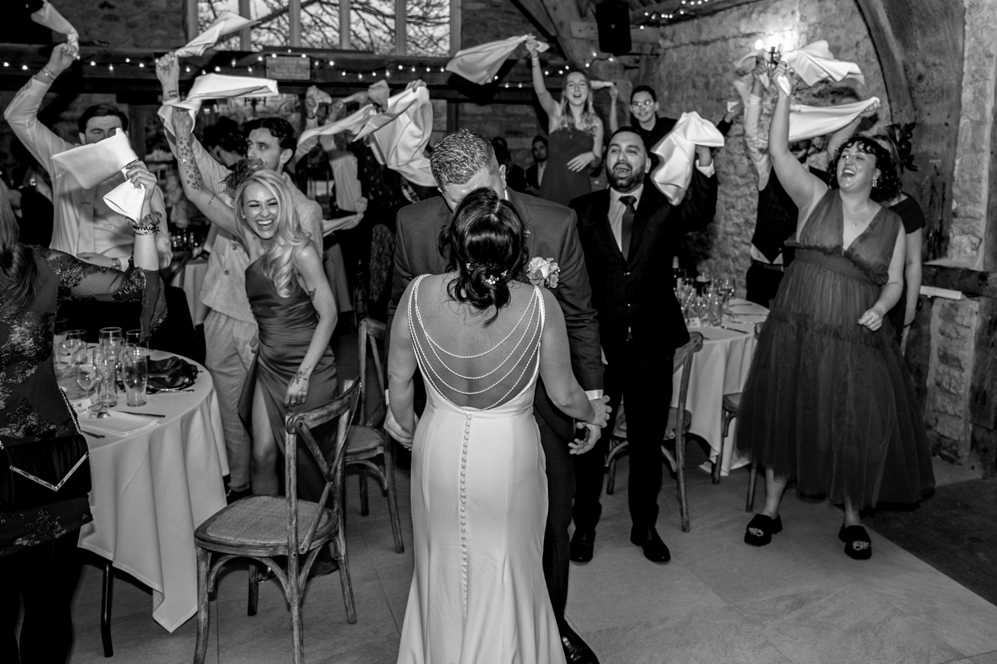 Black and white shot of bride and groom entering reception with guests waving napkins at Notley Tythe Barn