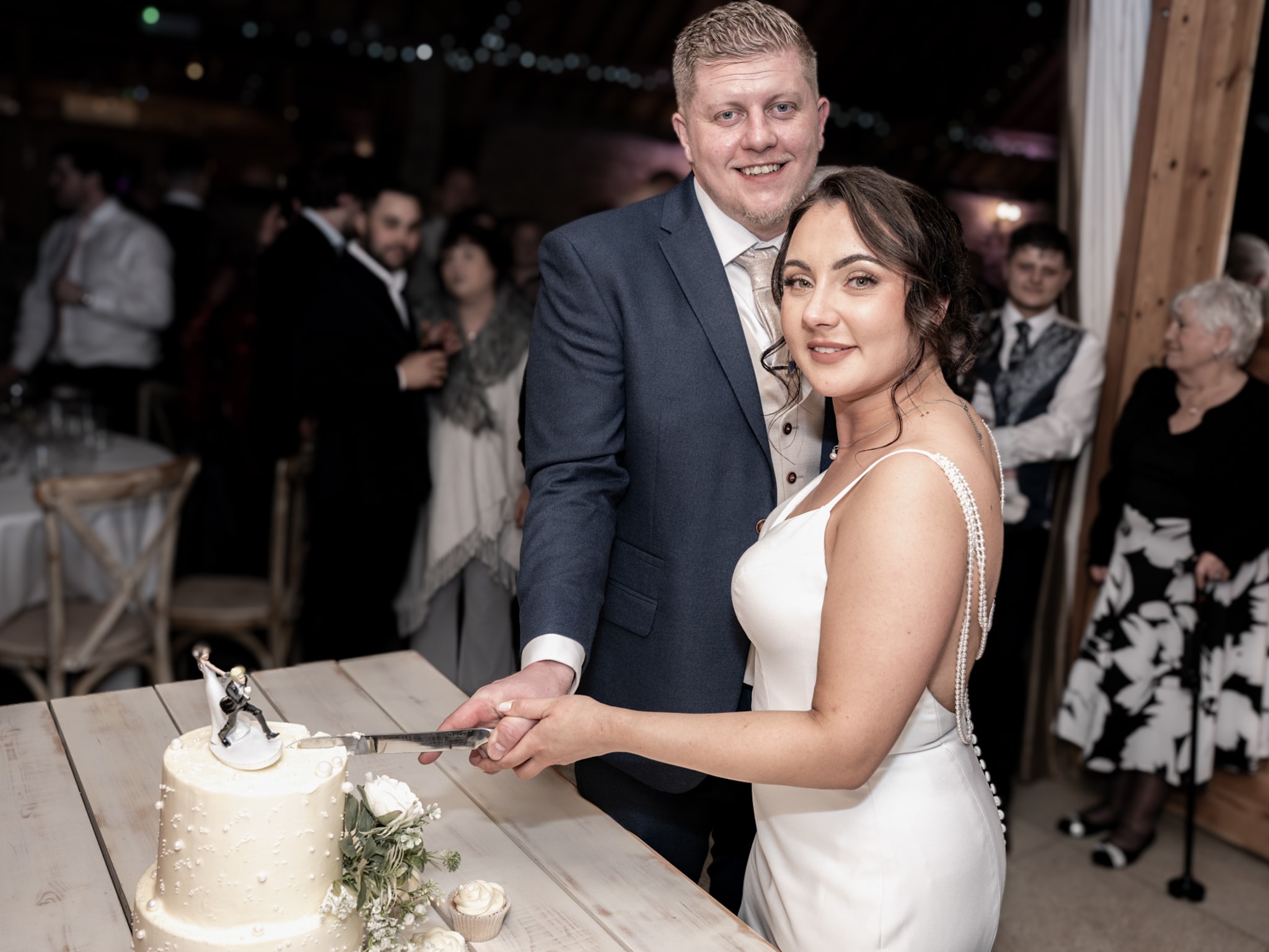 Bride and groom cutting their wedding cake together at Notley Tythe Barn reception with guests watching