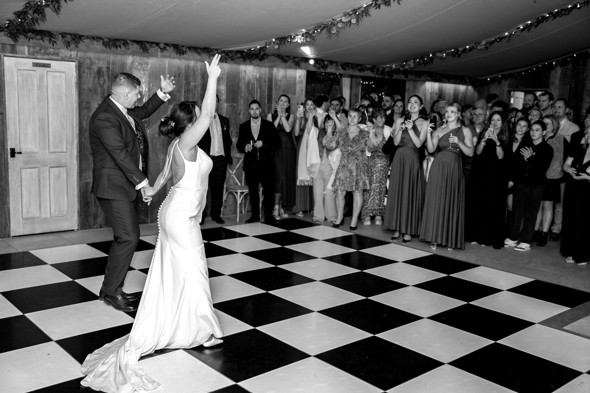 Bride and groom first dance black and white on checkered floor with guests watching at Notley Tythe Barn