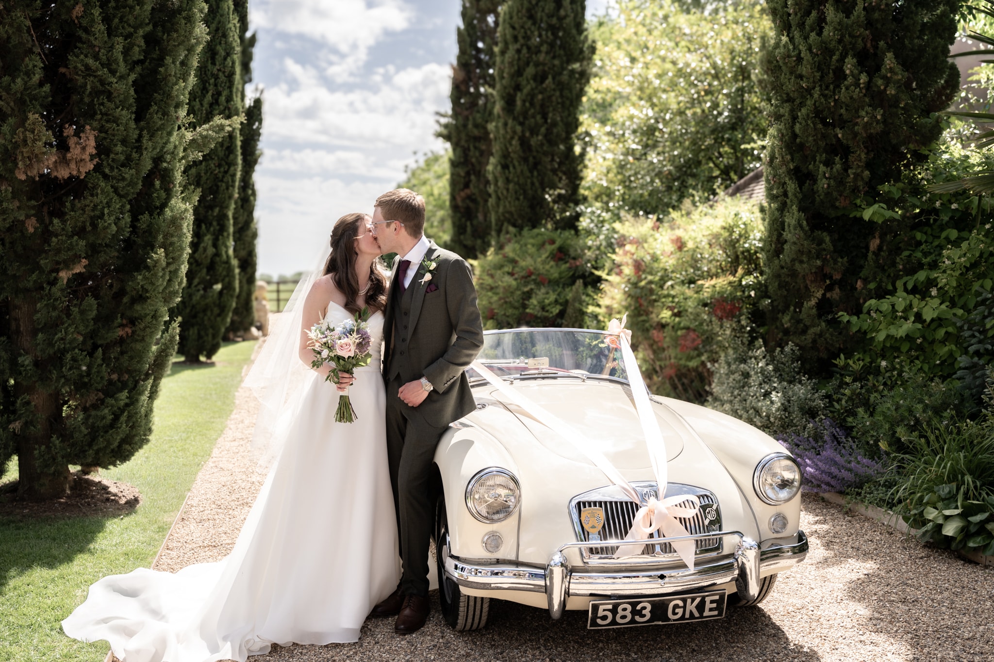 Bride and groom kissing by vintage car at Notley Tythe Barn wedding