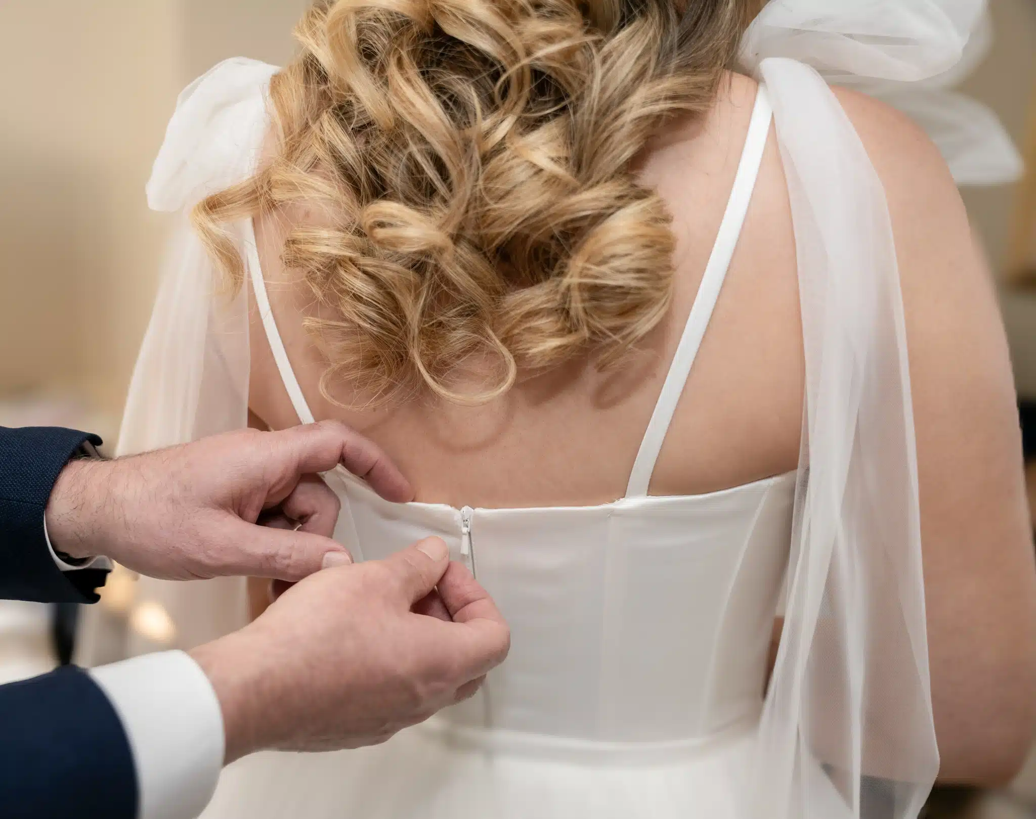 mans hands doing up the back of wedding dress