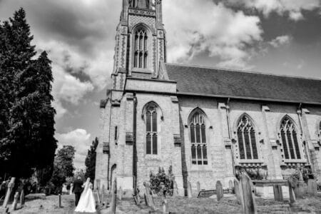 black and white image of newlyweds walking towards all saints church marlow