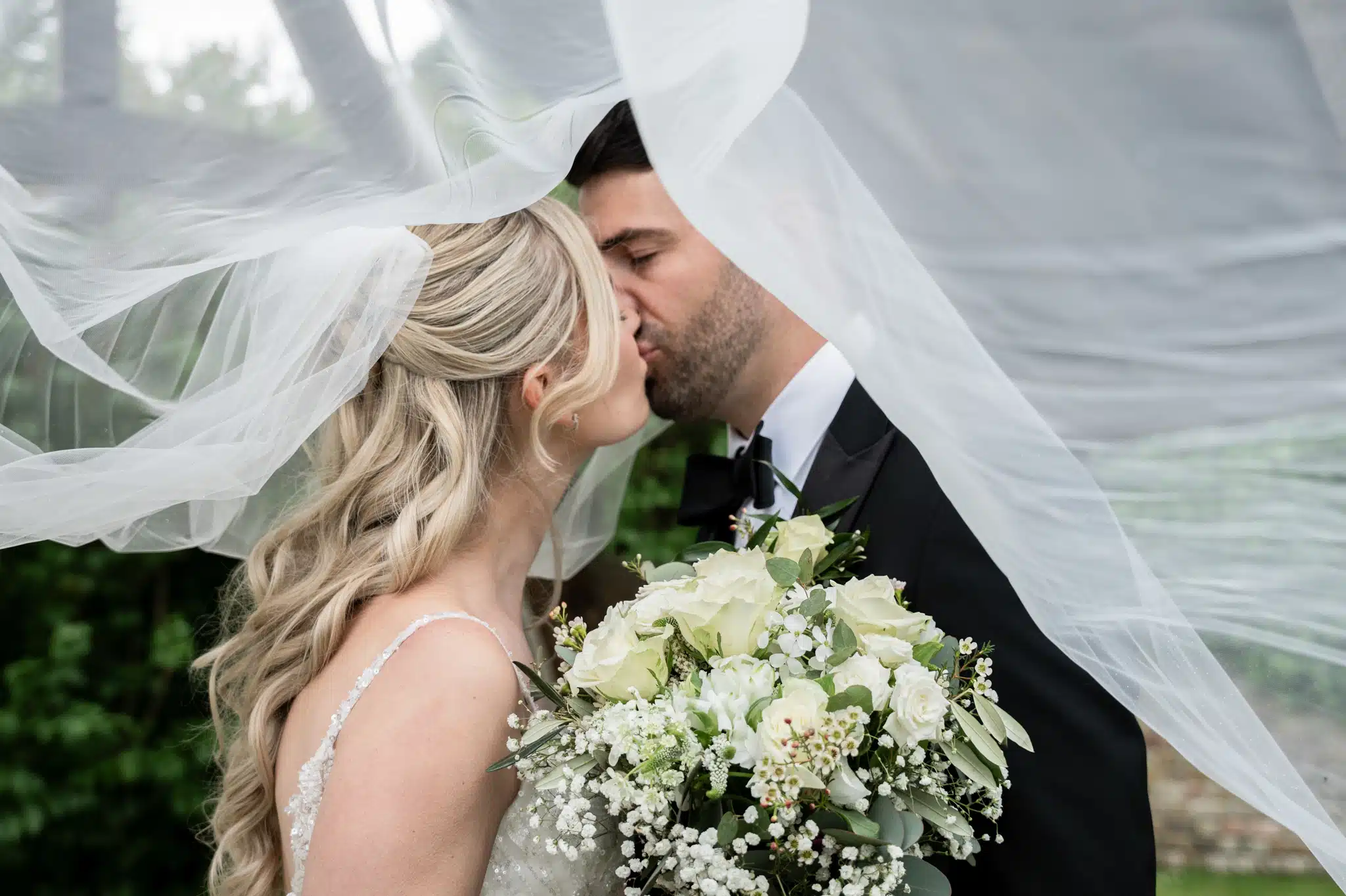 Bride and groom kissing under white veil
