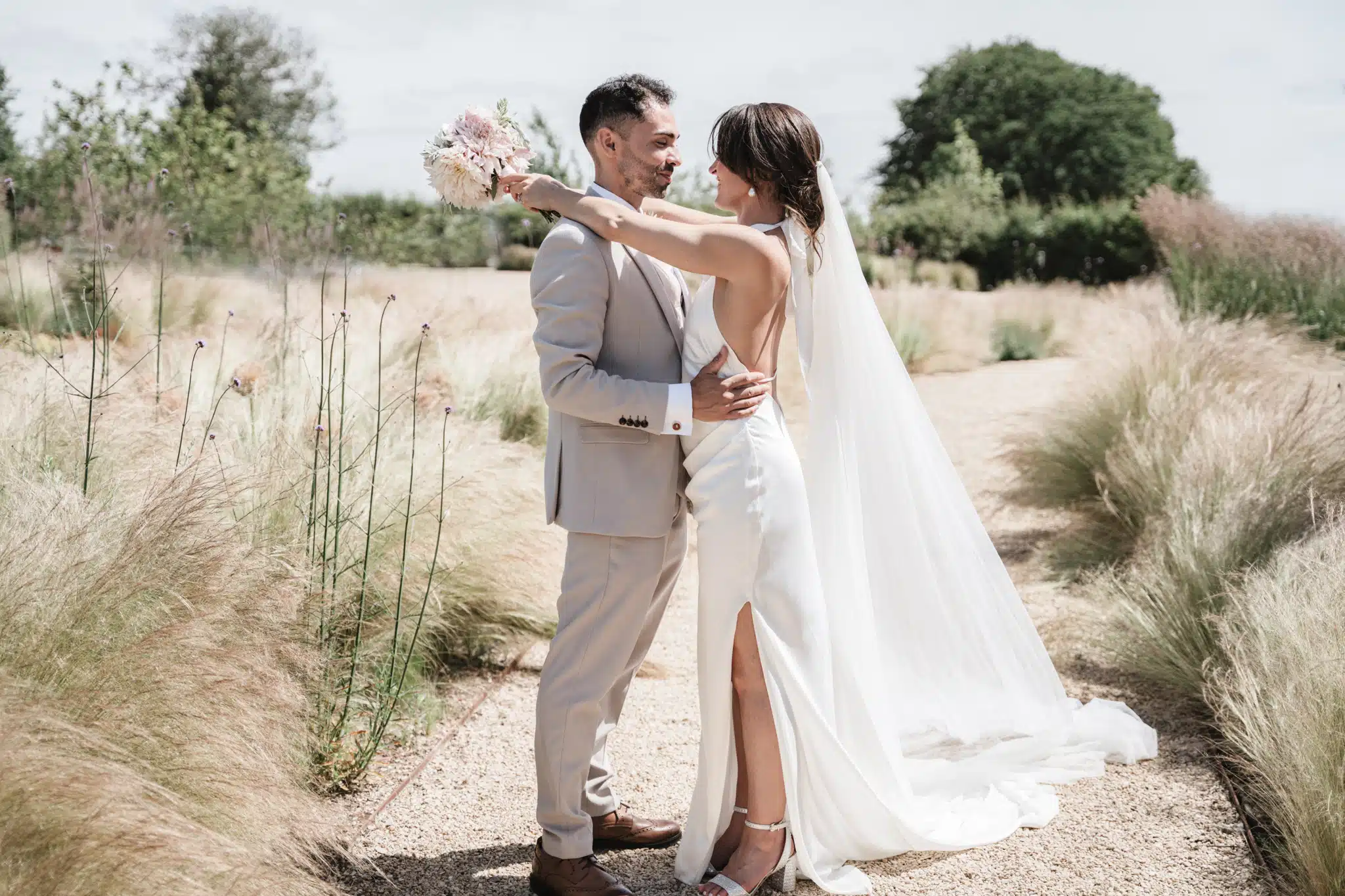 bride and groom embracing in field bride has pink bouquet