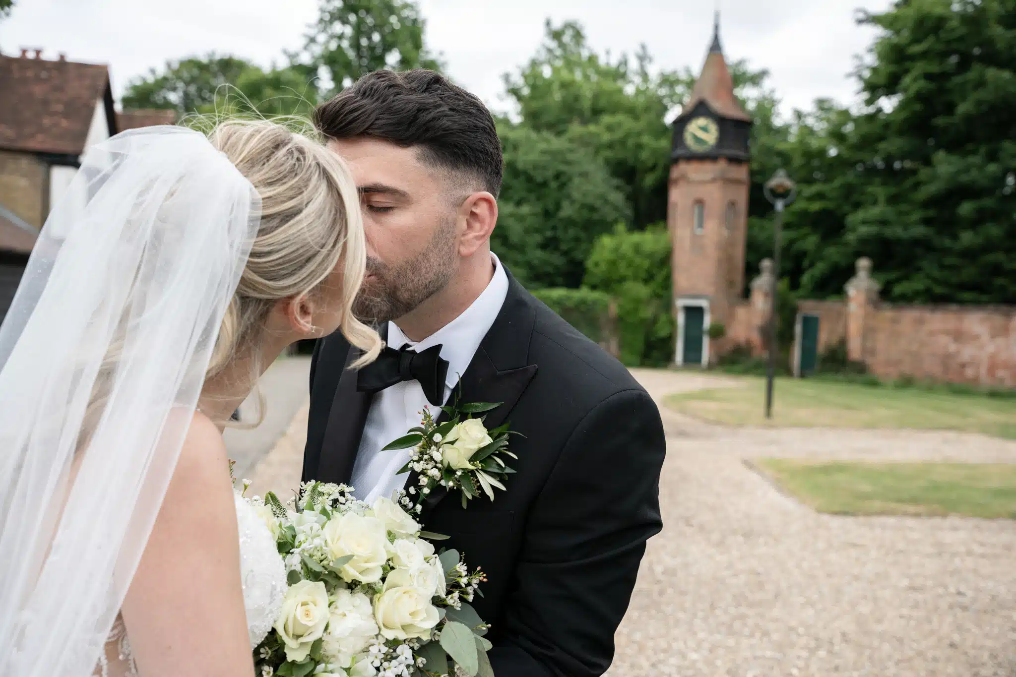 bride and groom kissing in front of clock tower at Tudor Barn